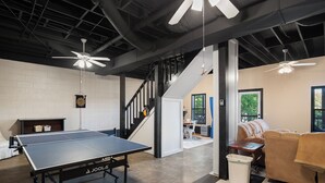 Taula de ping-pong en una habitació amb terra de pissos enrocats, ventiladors de sostre i una escala.