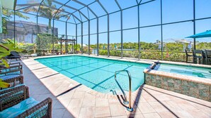 A covered swimming pool with clear blue water, surrounded by wicker lounge chairs and a glass enclosure.