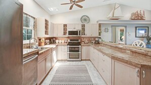 A modern kitchen with a central island, stainless steel appliances, and a ceiling fan.