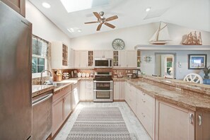 A modern kitchen with a central island, stainless steel appliances, and a ceiling fan.