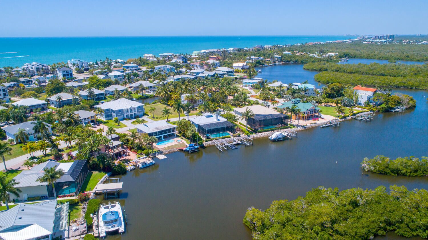An aerial view of a coastal residential area with houses, a marina, and a clear view of the ocean.