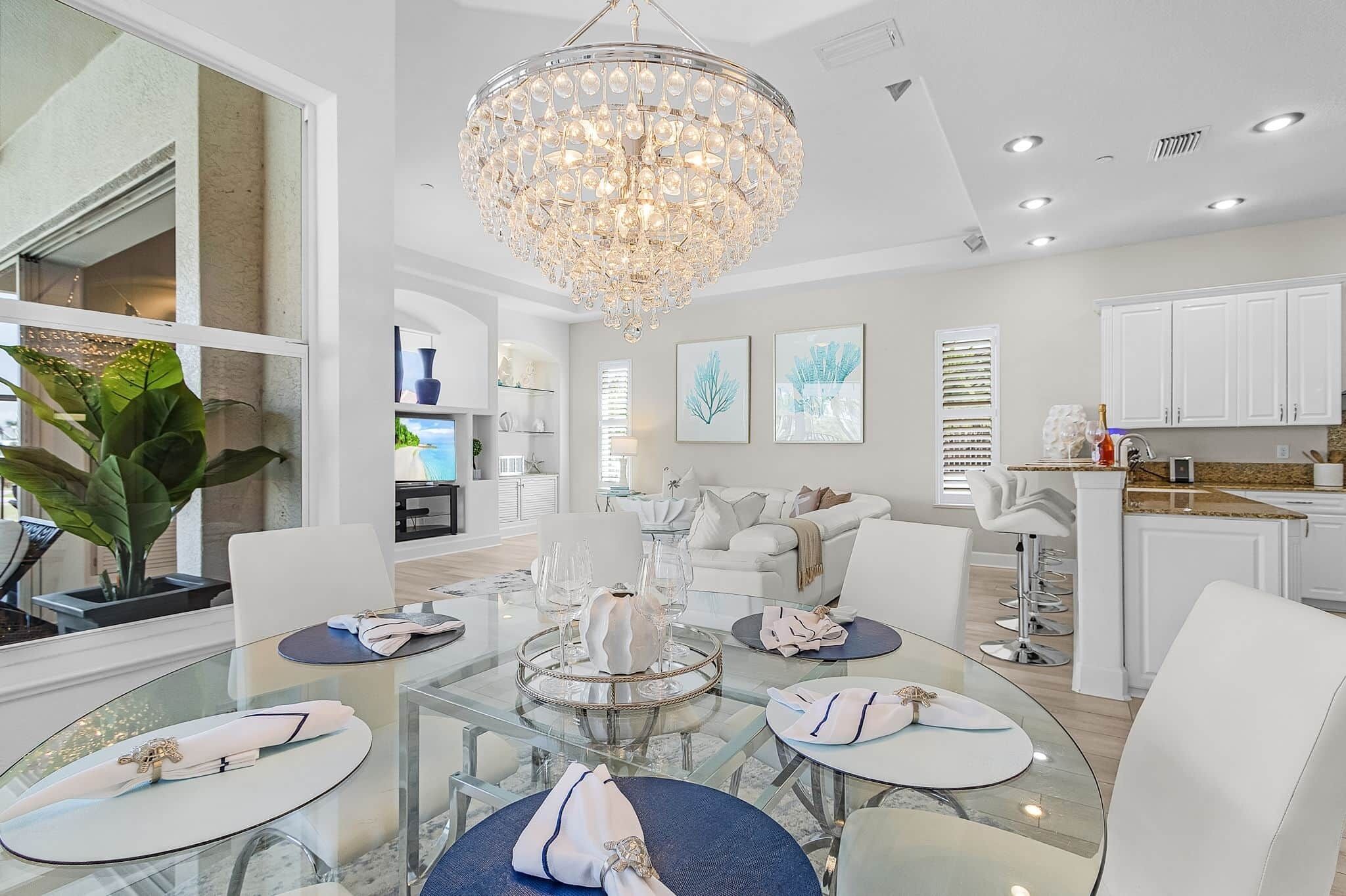 A modern dining area with a glass table, white chairs, and a crystal chandelier.