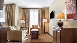Habitación de hotel con sofá, sillón, reposapiés, escritorio, lámpara y un cartel en la pared.