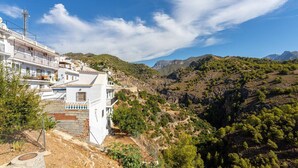 A white building with balconies, surrounded by a mountainous landscape and clear skies.