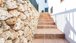 A stone wall beside a staircase leading to a white building with a window and a door.