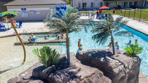 A pool area with palm trees, a lifeguard tower, and a building in the background.