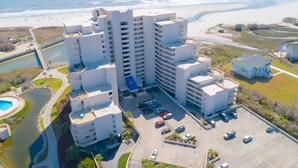 A high-rise hotel with multiple balconies, a parking lot, and a beach view.