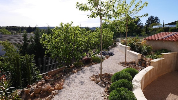 A landscaped garden with a gravel path, trees, and a stone wall.