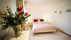 A bedroom with a bed, a nightstand, a vase with flowers, and a window with curtains.