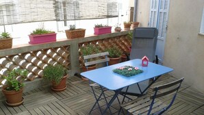 Une terrasse en bois avec une table et des chaises bleues, entourée de plantes en pot et d’une clôture à treillis.