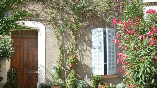 Un bâtiment avec une porte en bois, des plantes en pot et une fenêtre avec des volets.