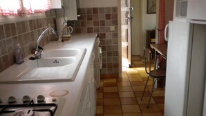 Una cocina compacta con un lavamanos, estufa y comedor con una silla.