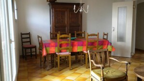 Un comedor con mesa y sillas de madera, mantel colorido, candelabro y puerta con panel de vidrio esmerilado.