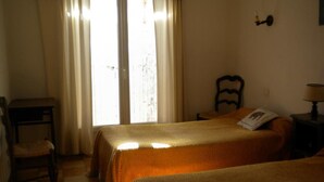 Una habitación con dos camas, una silla, una lámpara y un ventanal con cortinas.