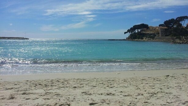 A beach with clear turquoise water, sandy shore, and a rocky cliff with trees. - Renecros 1 à 30 m de la mer (BANDOL)