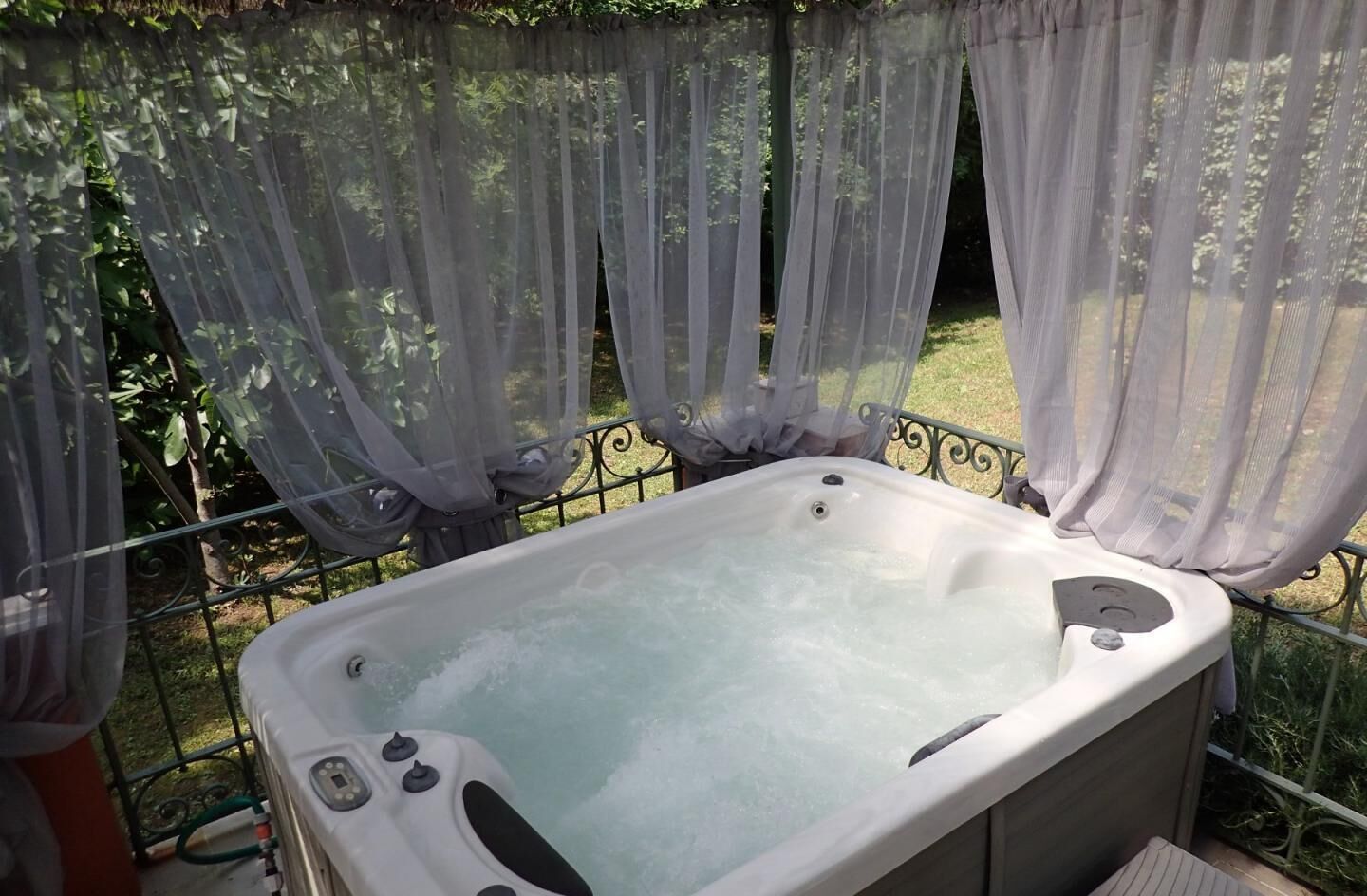 Un bain à remous installé à l’extérieur, entouré d’une clôture en métal et agrémenté de rideaux vaporeux.