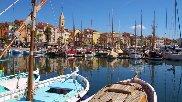 A marina with multiple boats docked, a prominent church with a bell tower, and colorful buildings along the waterfront. - Piscine Chauffée Privée - Parc Régional Naturel St (EVENOS)
