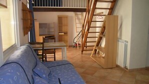 Ein Zimmer mit einem blauen Sofa, einer Holzleiter, einem Tisch und einem Bücherregal.