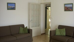 A room with two brown sofas, a white door with glass panels, and two framed pictures on the walls. - Le Bastidon des Tilleuls (LE BEAUSSET)