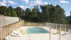 A fenced outdoor swimming pool with a stone border, surrounded by trees and a clear sky. - Le Bastidon des Tilleuls (LE BEAUSSET)