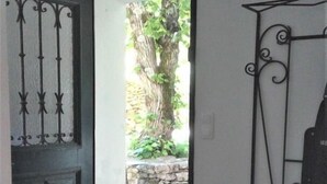 An interior hallway with a tiled floor, a dark door with decorative metalwork, and a metal rack with a coat hanging on it. - Le Bastidon des Tilleuls (LE BEAUSSET)