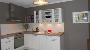 Una cocina moderna con armarios blancos, una campana extractora de acero inoxidable, horno integrado y un escurreplatos rojo.