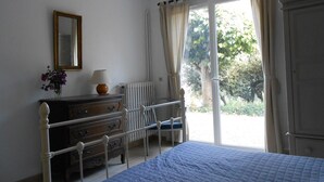 Un dormitorio con cama, cómoda, silla, radiador, ventana con cortinas y espejo en la pared.