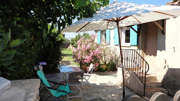En terrasse med et bord, stole, en stor parasol og en trappe til en bygning med blå skodder.