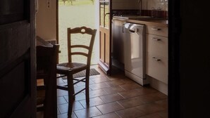 Een keuken met een vaatwasser, kastjes en een stoel, vlakbij een deur met uitzicht op een grasveld.