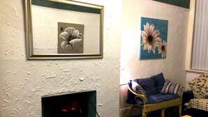 A living room with a fireplace, a framed floral artwork, a blue and purple chair, and a wooden coffee table. - 6 Person - 1 - Bed Apartment in Blackpool (Blackpool)