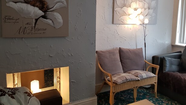 A room with a large floral painting, a wicker chair with cushions, a lamp, and a sofa. - 6 Person - 1 - Bed Apartment in Blackpool (Blackpool)