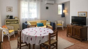 A living room with a round table, sofa, chairs, a TV, and an air conditioning unit. - Les Volets Bleus - LA Garde Freinet (LA GARDE FREINET)