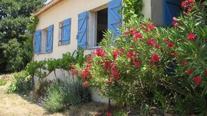A building with blue shutters, a stone wall, and a garden with red flowers. - Les Volets Bleus - LA Garde Freinet (LA GARDE FREINET)