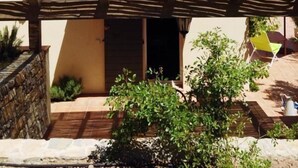 Une maison dotée d’un patio couvert, d’un mur en pierre et d’un petit jardin planté.