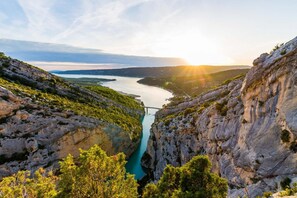 Surrounded by lush greenery and rocky cliffs, this serene landscape features a tranquil river and a picturesque bridge.