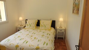 Un dormitori amb un llit, dues taules de nit, una finestra i un quadre a la paret.