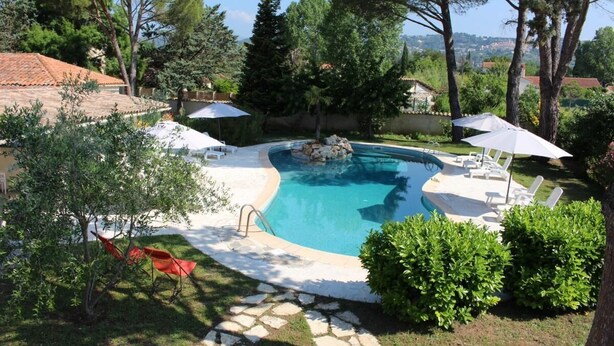 A swimming pool with a stone deck, surrounded by greenery and trees, with lounge chairs and umbrellas. - La Cigale Verte à Callian (CALLIAN)