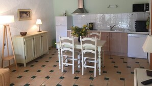 A compact kitchen with a dining area, featuring a central table with chairs, a small refrigerator, a microwave, and a sink. - La Cigale Verte à Callian (CALLIAN)