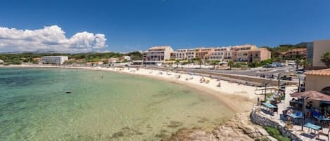 A coastal hotel with a beach view, clear waters, and a row of buildings along the shore.