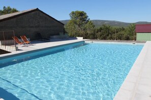 A swimming pool with clear blue water, surrounded by a white deck and a few orange lounge chairs. - Le Domaine de la Crèche (NANS LES PINS)