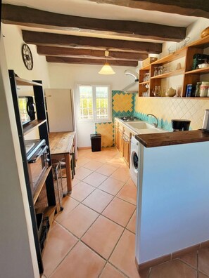 Une cuisine avec un plan de travail en bois, un lave-linge et un sol carrelé.