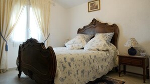 Ein Schlafzimmer mit einem hölzernen Bett, floralem Bettzeug, einem Nachttisch mit Lampe und einem Fenster mit Vorhängen.