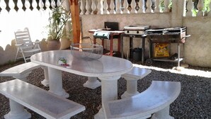 Eine Außenpatio mit einem runden Tisch und Bänken, umgeben von Kies, mit einem weißen Zaun und Topfpflanzen im Hintergrund.