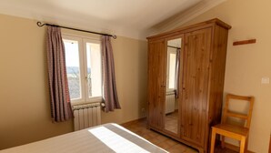 Ein Schlafzimmer mit Bett, Holzschrank, Stuhl und einem Fenster mit Vorhängen.