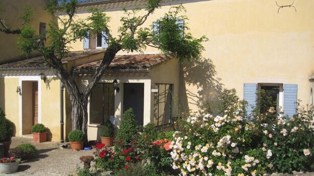 Ein Gebäude mit gelber Fassade, mehreren Eingängen und einem Garten mit verschiedenen Pflanzen und Blumen.
