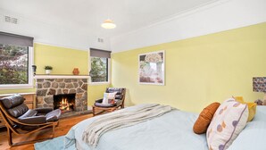 A cozy room with a stone fireplace, a comfortable leather chair, a bed with pillows, and a window with a view of trees. - Pet Friendly - Retro Beach Babe 100 metres to the beach (Tootgarook)