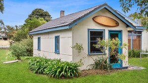Une petite maison de plain-pied, dotée d’un toit en pente, d’un porche à l’avant et d’un petit jardin agrémenté de plantes vertes.