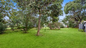 Une cour bien entretenue, recouverte de gazon, avec de grands arbres, un petit arbuste et une citerne d’eau en métal.