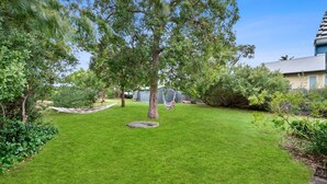 Un jardin bien entretenu avec un hamac, un petit parterre de fleurs circulaire et une variété d’arbres et d’arbustes.