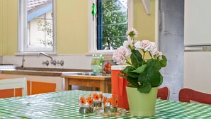 Un coin repas avec une nappe à carreaux verts et blancs, un vase rempli de fleurs roses et de petits verres décorés de fleurs oranges.